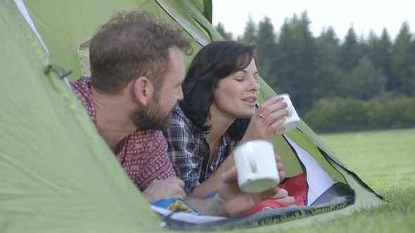 Couple lying in dome tent and drinking coffee