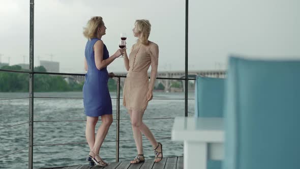 Wide Shot, Smiling Elegant Women Drinking Red Wine on River Bank. Portrait of Charming Caucasian alt