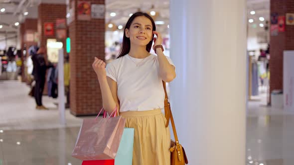 Amazed Young Woman with Paper Bags in Hand Looking at Glass Showcase in Shopping Mall alt