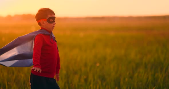 A Boy in a Superhero Costume at Sunset Runs Across the Field Laughing and Smiling alt