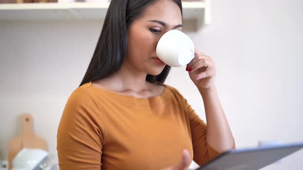 Young woman relaxing standing in kitchen and using digital tablet.