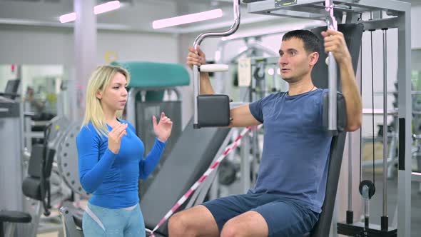 The trainer tells the client a skinny guy how to do the exercise on machine alt