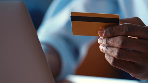 Serious man pays online holding credit card and typing on white laptop alt