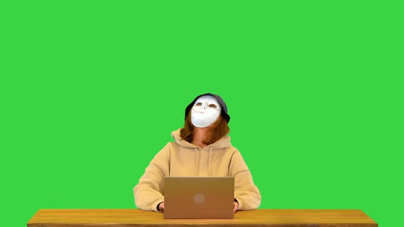 Hacker Girl in Anonymous Mask and Hoodie Typing on Laptop Coding Virus Software for Fraud Attack on
