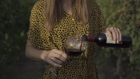 Woman Pours Red Wine Into a Glass in a Vineyard