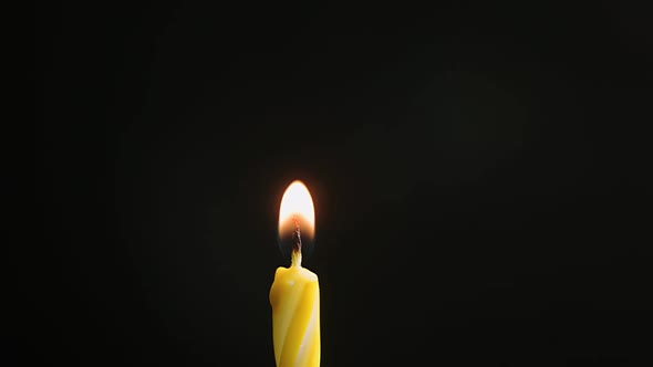 Single Big Yellow Candle Flame Lights and Extinguish Isolated on a Black Background Slow Motion