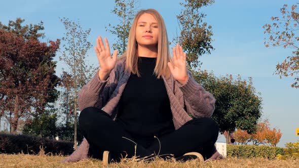Young European Woman Meditating Outdoors Sitting in Lotus Position in the Park alt