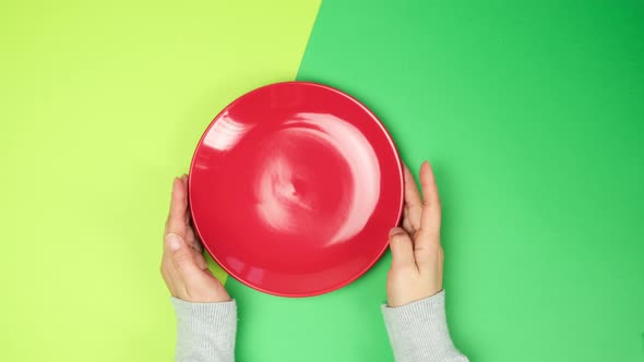 female hand puts on green surface an empty round red ceramic plate