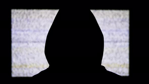 Silhouette of Man's Head in Hood Is Watching White Static Noise and TV Interference. alt