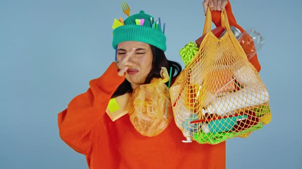 Woman holding  package with garbage and showing stinky emotion.