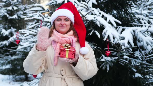 A woman waves and throws a gift looking at the camera at the Christmas tree in the winter park