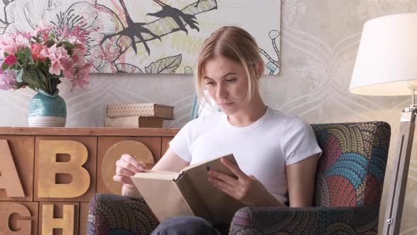 A Young Blonde Woman Reads A Book Novel, Hand Turns The Page Of The Book alt