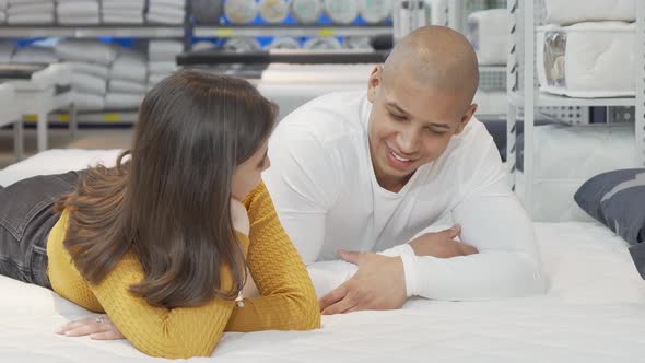 Young Couple Talking While Lying on a New Bed at Furniture Store