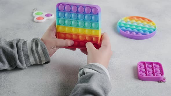 Unrecognizable Child Pushes Bubbles on Colorful Poppit Toy with Fingers at Table