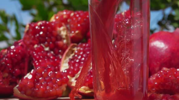 Fresh Pomegranate Juice Wave is Flowing Into a Jug on the Background of Sky alt