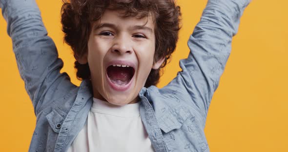 Excited Young Boy Enjoying Win, Raising Hands and Shouting, Orange Studio Background, Close Up alt