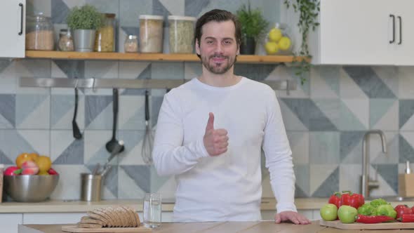 Young Man Showing Thumbs Up While Standing in Kitchen alt