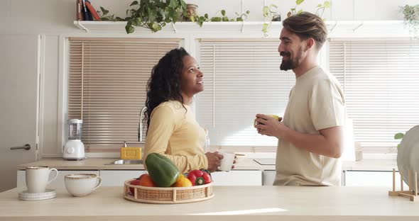 Happy Multiethnic Heterosexual Young Couple Having Coffee or Tea in Apartment alt