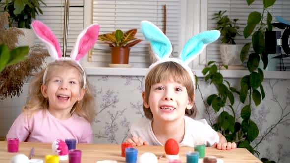 a Little Girl and a Boy with Easter Bunny Ears Jump Out From Under the Table and Laugh Chicken Eggs alt