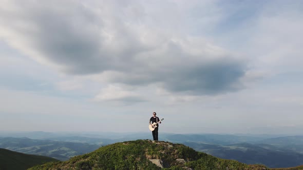 Aerial View of Young Guy Musician Playing Acoustic Instrument in the Mountains