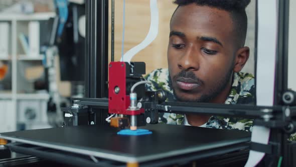 Smiling Young Man Looking at 3D Printer Printing Plastic Model in Office alt