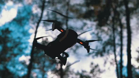 Drone with a Camera Hovers in the Air. Flies Above the Ground in the Forest. Slow Motion alt