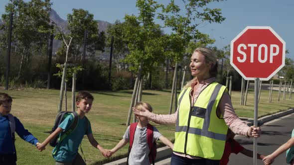 Woman with Hi-vest holding stop sign while group of kids cross the road alt
