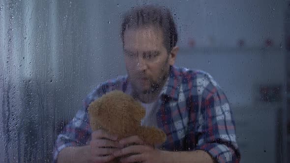 Lonely Male Holding Teddy Bear Behind Rainy Window, Missing Child After Divorce alt