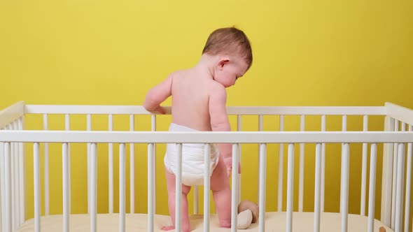 Infant baby boy is standing with his back in the crib, yellow studio background