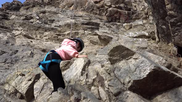 Girl is Engaged in Rock Climbing on a Steep Cliff alt