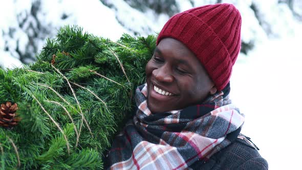 Latin Hispanic Man in Red Hat Scarf and Stylish Coat Carrying Eco Reusable Pine Tree From Outdoor alt