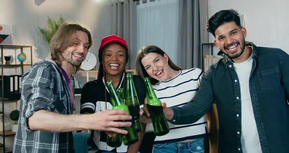 Friends which Clinking Bottles of Beer while Looking at Camera During Home Party alt