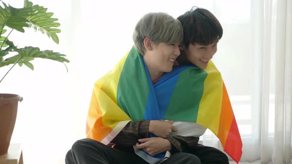Asian loving gay couple cuddling, putting on LGBT rainbow flag to cover shoulder alt