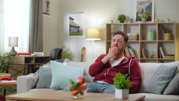 Man Sitting at Home on the Couch and Biting a Apple alt