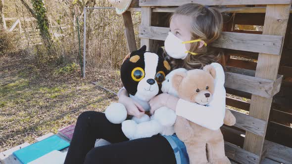 Slow motion shot of girl with mask playing with her teddies in garden alt