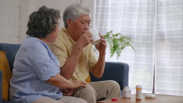 Asian senior couple elderly taking pills, drinking water in the living room at home.