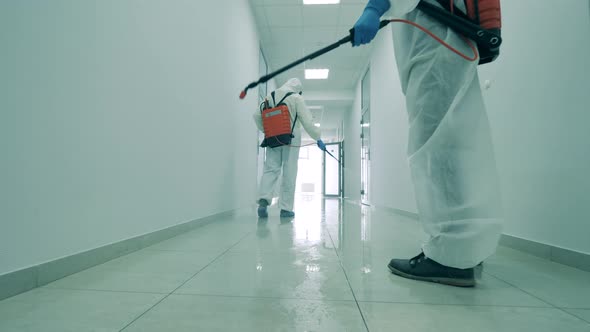 People in Hazmats Clean Hallway, Using Sprayers. alt