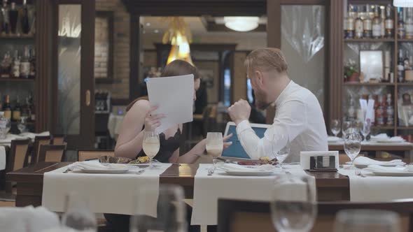 Portrait Cute Young Woman Sit with Papers on the Table in Restaurant with a Confident Bearded Man alt
