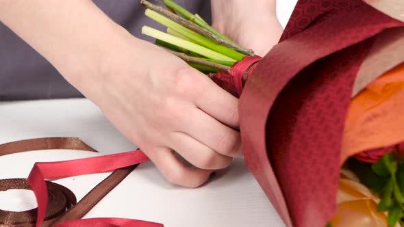 Florist Tying a Bow of Ribbon on a Bouquet of Flowers. White. Close Up alt