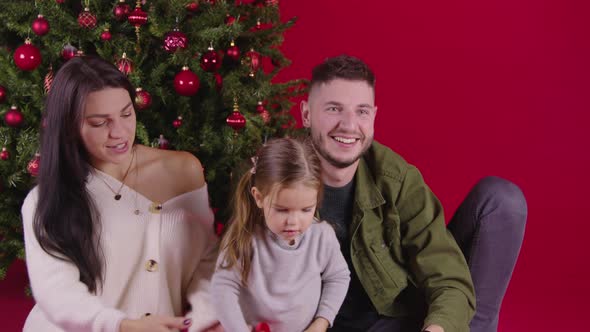 Happy Family Sorting Christmas Gifts Near Xmas Tree on Red Festive Background