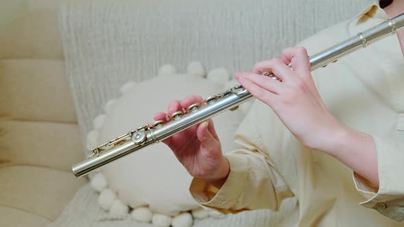 A woman hand with a flute is playing at home on the sofa in the living room, close-up