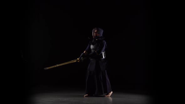 Strong Kendo Guru Practicing Martial Art with the Bamboo Bokken on Black Background. alt