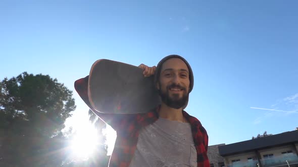 Portrait of a Smiling Skateboarder with a Beard Who Carries a Skate on His Shoulder