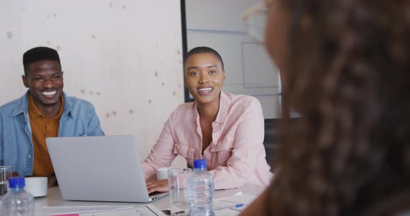 Three happy diverse male and female creative colleagues having coffee and laughing at meeting alt
