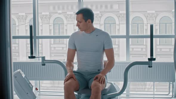 Modern Gym - a Guy Sitting Down on the Training Apparatus and Waiting for When It Will Be Possible alt