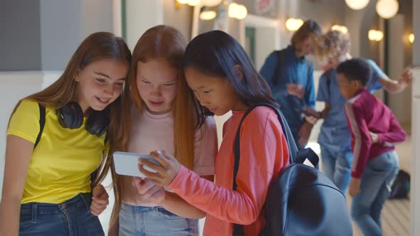 Three Multiethnic School Girlfriends Using Smartphone in Corridor During Break alt