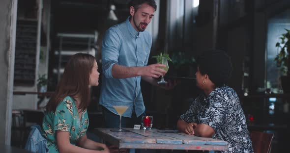 Waiter delivering coctails to the young couple on dinner date alt