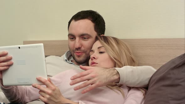 Young Couple Lying on the Bed Make Shopping Over the Internet Using Tablet alt