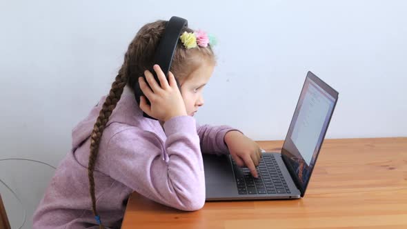 Little Girl on Distance Learning Sits in Headphones