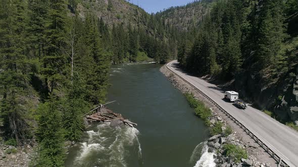 Drone Flying Up Pacific Northwest River With Camper Rv Towing Boat On Mountain Highway